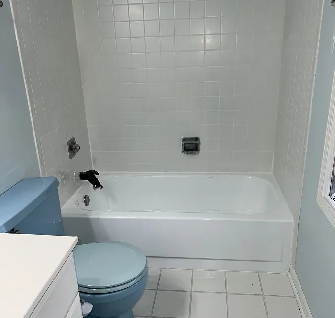Bathroom with white tiled walls, a white bathtub, and a light blue toilet.