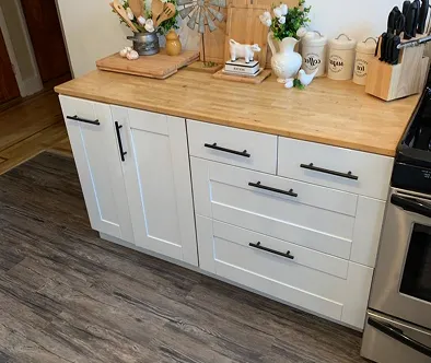 White kitchen cabinets with wooden countertop and various kitchen decor items.