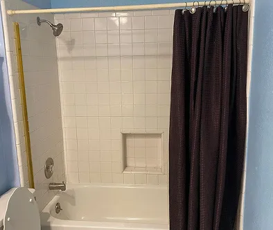 Bathroom with white tiled shower and tub, dark brown shower curtain, and toilet.