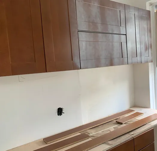 Kitchen cabinets installed above a white backsplash with wood planks laid out on the counter.