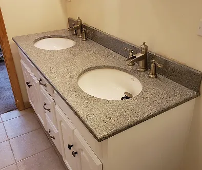 Double vanity with white cabinets and granite countertop with two sinks and faucets.