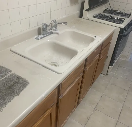 Kitchen sink and countertop with wooden cabinets and a stove in the background.