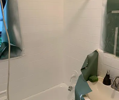 Bathroom renovation with white tiled walls and bathtub covered in protective sheeting.