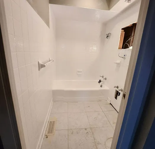 White tiled bathroom with a bathtub, shower, and unfinished wall section.