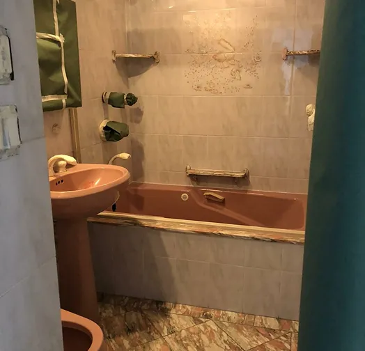 Pink sink and bathtub in a tiled bathroom with green towels on a rack.
