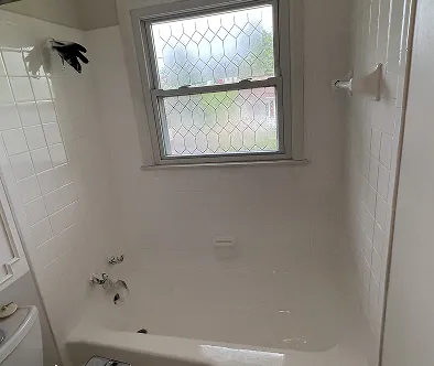 White bathtub with tiled walls and a window with decorative glass