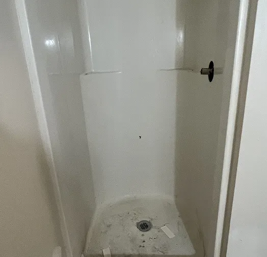 White shower stall with drain and shower head fixture.