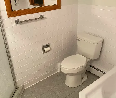 Bathroom with white tiled walls, toilet, and mirror.
