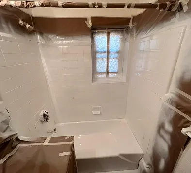 White bathtub and tiled walls covered in plastic sheeting for painting.