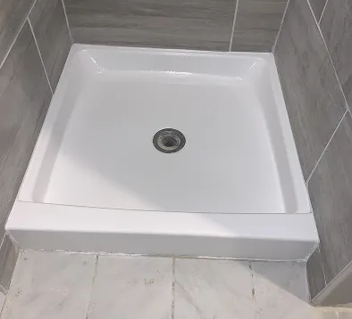 White rectangular shower base with a drain in the center, surrounded by gray tiled walls and white tiled floor.