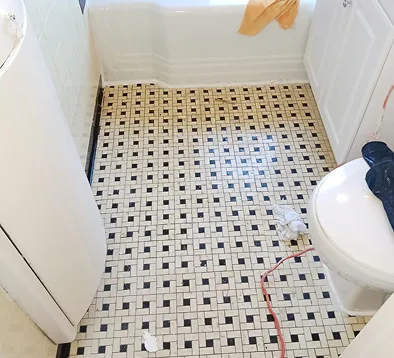 Bathroom floor with black and white mosaic tile, toilet, and bathtub.