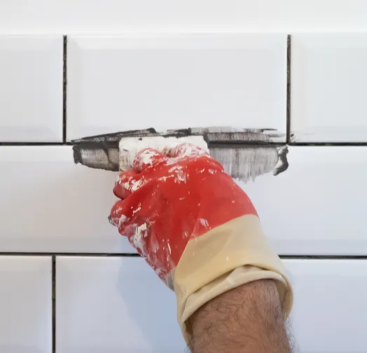 Hand in red glove applying grout to white subway tiles.