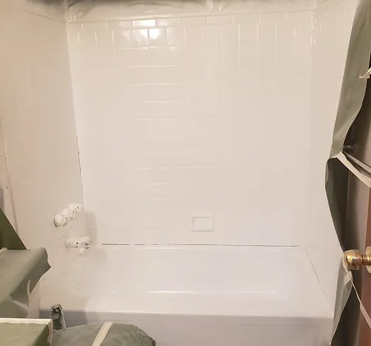 White bathtub and tiled shower walls covered with plastic sheeting for protection.