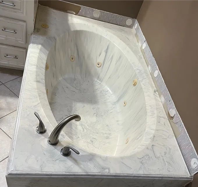 White whirlpool bathtub with chrome fixtures and marble-patterned surround