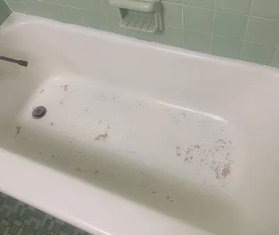 White bathtub with chipped enamel and green tiled walls
