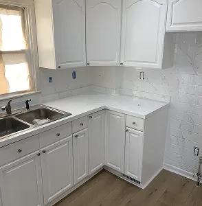 White kitchen cabinets and countertops with a double sink and window.
