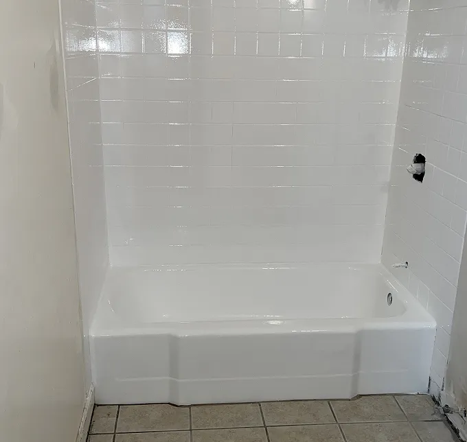 White bathtub with white tiled walls and beige tiled floor