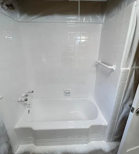 White bathtub and tiled shower walls covered with plastic sheeting.