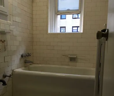 Bathroom with white subway tile, bathtub, and window showing building exterior