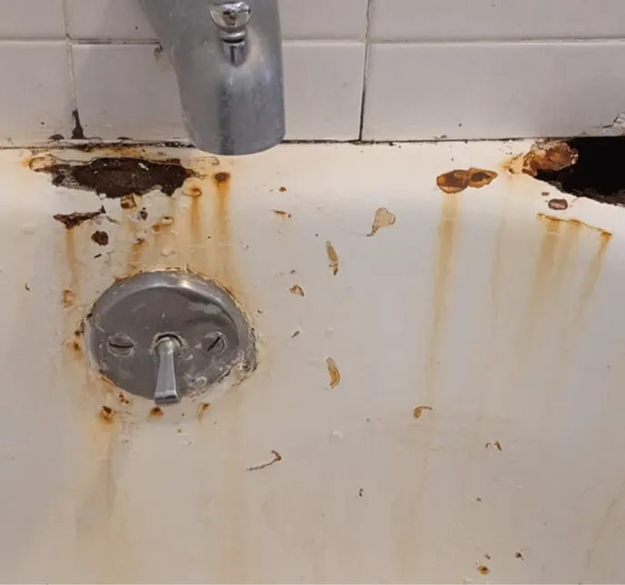Rusted and peeling bathtub with chrome faucet and drain control.