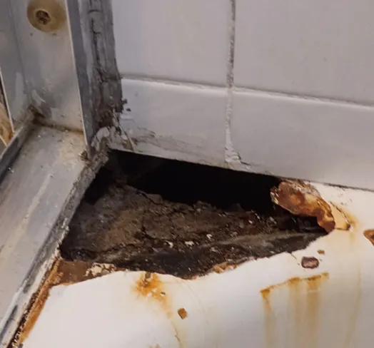 Damaged bathtub corner with rust and debris