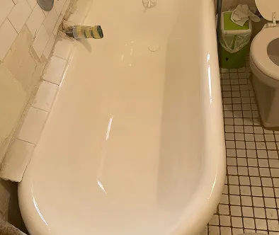 White bathtub with a toilet and green trash can in a tiled bathroom.